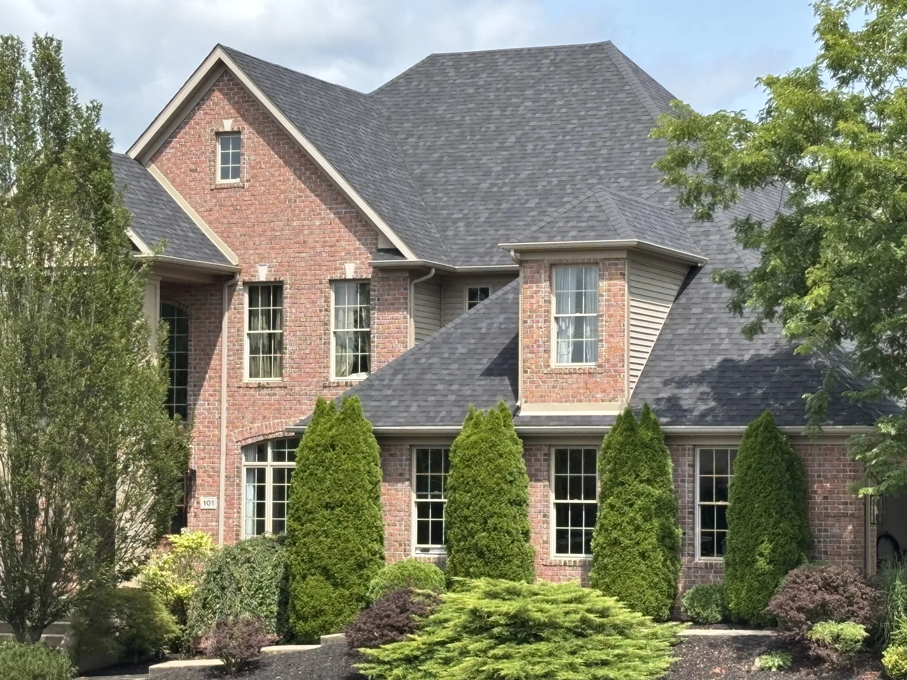 Close view of the new charcoal architectural shingle roof, gables, and dormers on a large brick home by West Penn Exteriors
